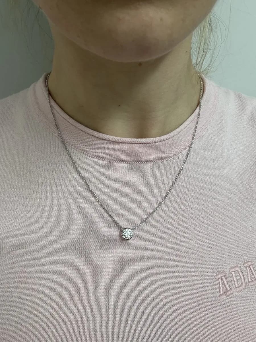 A solitaire diamond pendant in a bezel, worn on a fine chain